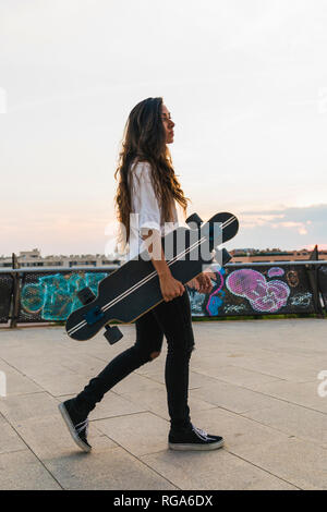 Giovane donna a piedi con lo skateboard in città Foto Stock