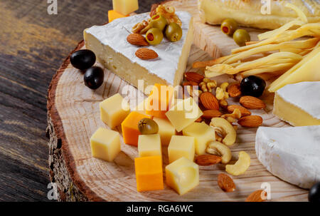 Diversi tipi di formaggio, olive e dadi assortiti Sfondo legno formaggi assortiti Foto Stock