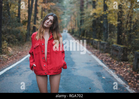 Ritratto di giovane donna in piedi sulla strada di campagna indossando giacca rossa Foto Stock