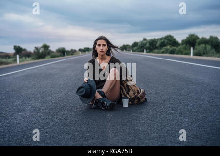 Ritratto di autostop giovane donna con zaino e bevanda seduto su lane