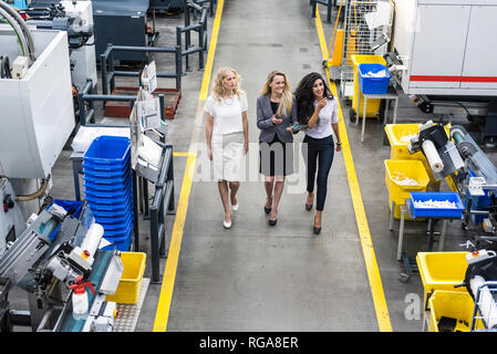 Tre donne sorridente con la compressa a piedi nella fabbrica negozio Foto Stock