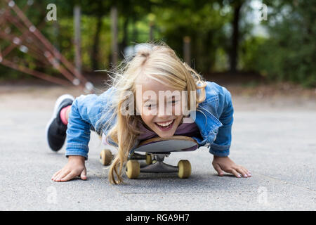 Ritratto di ridere ragazza bionda giacente sul suo skateboard all'aperto Foto Stock