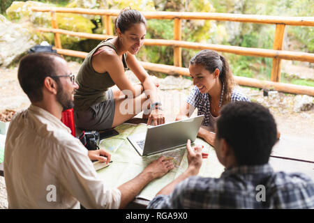 Gruppo di escursionisti seduti insieme la pianificazione di un percorso escursionistico usando la mappa e il computer portatile Foto Stock