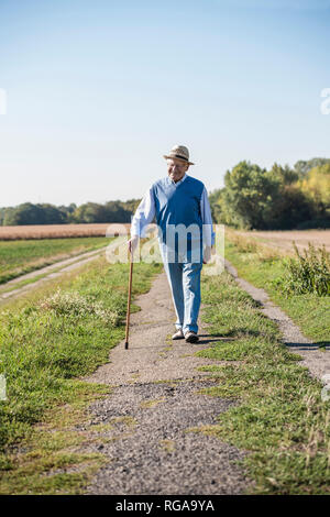 Senior uomo con un bastone da passeggio, passeggiate nei campi Foto Stock