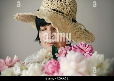 Felice madre con grande mazzo di peonie rosa dando da bambini. Felice Festa della mamma concetto. Bella donna anziano in hat in posa con molti peonia flo Foto Stock