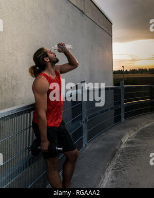 Giovane uomo acqua potabile dopo il training con manubri Foto Stock