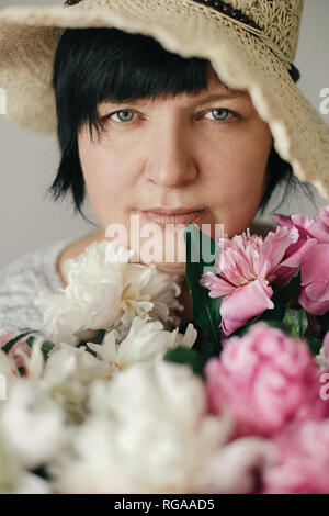 Bella donna di hat in posa con molti peonia fiori. Felice madre con grande mazzo di peonie rosa da bambini. Felice Festa della mamma concetto. Giornat Foto Stock