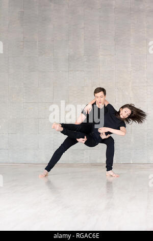 Coppia giovane in nero danza. Ballerini in azione su sfondo grigio. Giovane talento l uomo e la donna pratica di nuova danza. Foto Stock