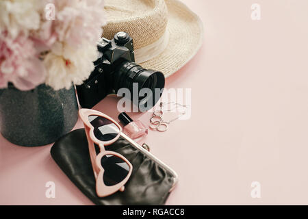 La Giornata internazionale della donna. Elegante girly immagine di rosa le peonie, macchina fotografica, occhiali da sole retrò, gioielli, smalto per unghie, cappello, portamonete sul pastello carta rosa Foto Stock