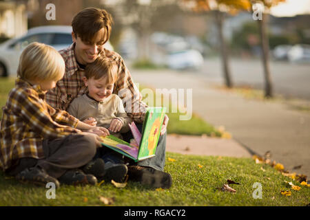 Padre e figli seduti sul prato storie di lettura. Foto Stock