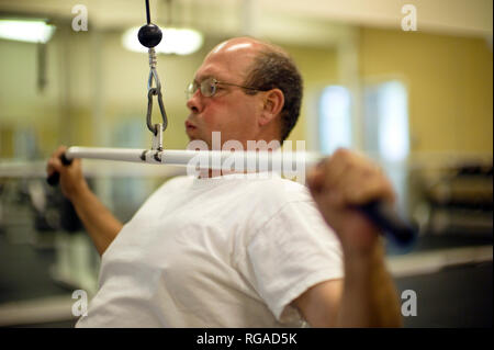 Uomo maturo espira come egli utilizza una laterale di pull-down macchina di peso in una palestra. Foto Stock