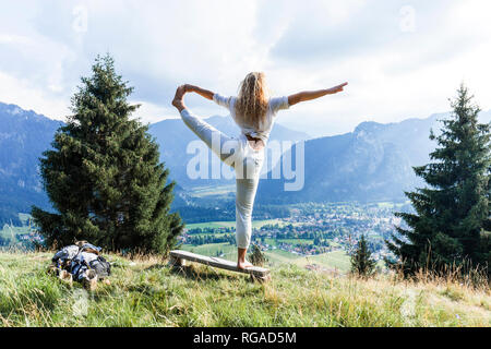 In Germania, in Baviera, Oberammergau, giovane donna fare yoga su banco sul prato di montagna Foto Stock