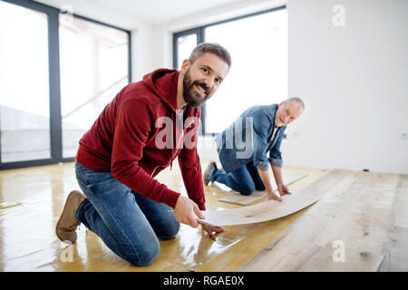 Una parte posteriore ed in pianta di uomo maturo con il suo anziano padre la posa di pavimenti in vinile, un nuovo concetto di casa. Foto Stock