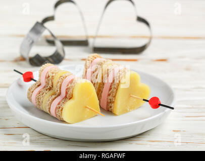 Mini sandwich di formaggio parmigiano prosciutto cotto il pane su spiedini di legno in forma di cuori. Il giorno di San Valentino. La prima colazione per i propri cari. Messa a fuoco selettiva e spazio di copia Foto Stock