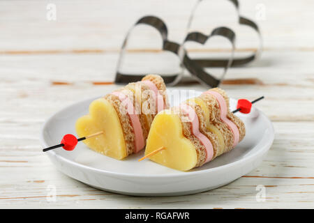 Mini sandwich di formaggio parmigiano prosciutto cotto il pane su spiedini di legno in forma di cuori. Il giorno di San Valentino. La prima colazione per i propri cari. Messa a fuoco selettiva e spazio di copia Foto Stock