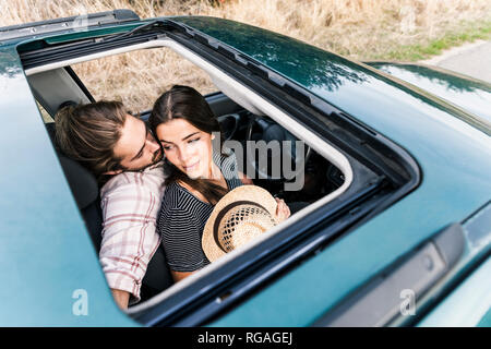 Affettuosa coppia giovane in una vettura vista attraverso il tettuccio apribile Foto Stock