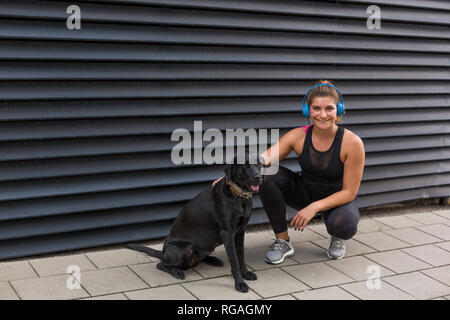 Ritratto di sorridente giovane donna con le cuffie e il suo cane all'aperto Foto Stock