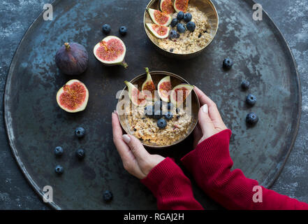 Donna di mani ciotola di porridge con fette di fichi, mirtilli e frutti di bosco essiccati Foto Stock