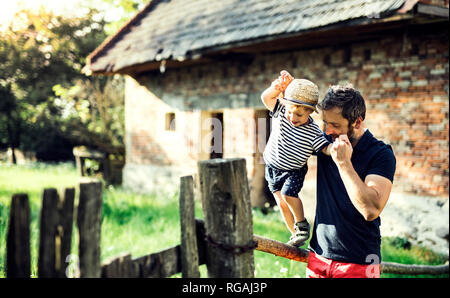 Padre assistere il suo piccolo figlio in equilibrio su una recinzione Foto Stock