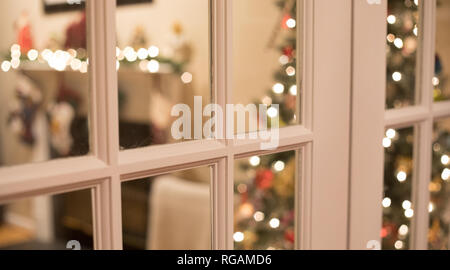 Un bokeh foto del peering attraverso il francese porta windows in un salotto decorato per il Natale. Foto Stock