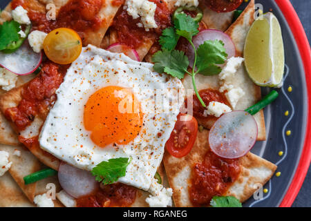 Colazione messicana: chilaquiles con uovo, avocado e verdure close-up su una piastra Foto Stock