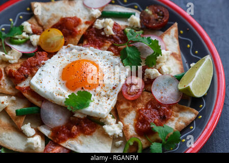 Colazione messicana: chilaquiles con uovo, avocado e verdure close-up su una piastra Foto Stock
