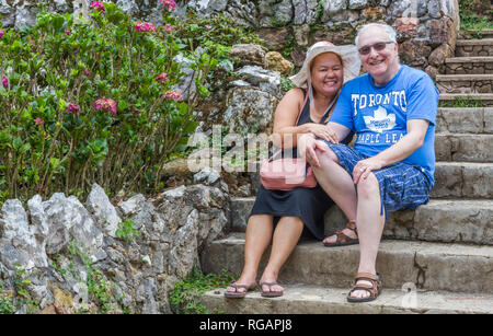 Piuttosto, sorridente donna filippina e marito canadese sedersi sui passi concreti di cui godono i bellissimi fiori a Camp John Hay a Baguio, Filippine. Foto Stock