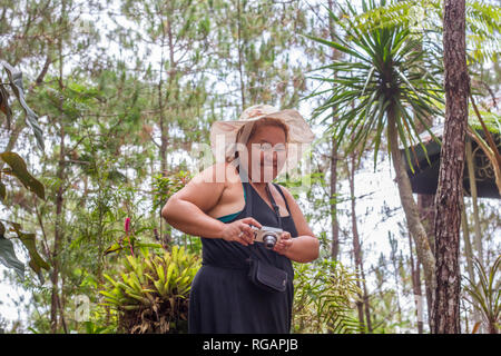 Sorridente, bella donna filippina si prepara a prendere le foto nel mezzo di alberi, arbusti e altre piante al bellissimo Camp John Hay a Baguio, Filippine. Foto Stock