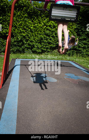 Due ragazze caucasion giocando su oscilla in un parco in un parco giochi con ombra Foto Stock