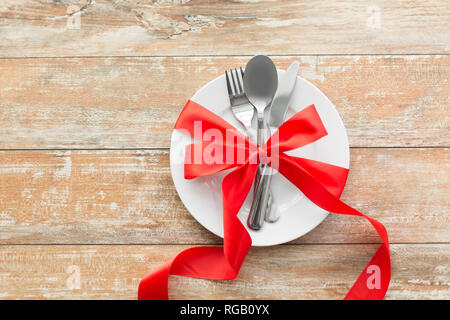 Posate legate con un nastro rosso sul set di piastre Foto Stock