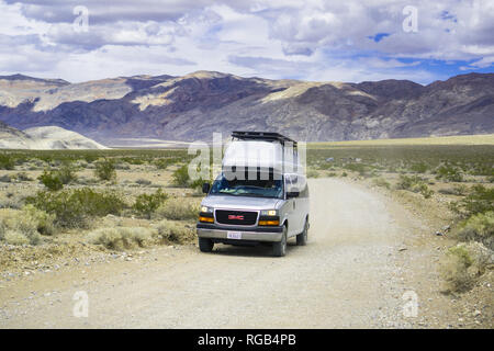 Maggio 27, 2018 Death Valley / CA / STATI UNITI D'AMERICA - modificati GMC minivan viaggia su una strada sterrata attraverso una zona remota della Death Valley; conversione standard v Foto Stock