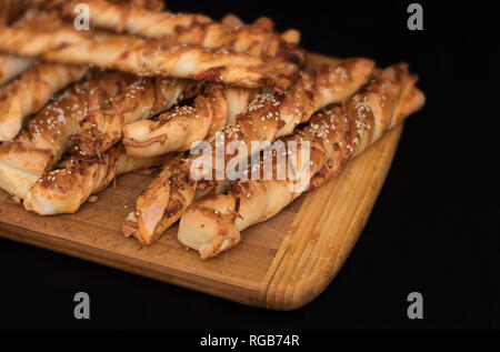 Twisted formaggio bastoncini di pane con prosciutto e i semi di sesamo su una tavola di legno su uno sfondo nero Foto Stock