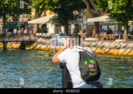 GARDA, Italia - Settembre 2018: Persona guardando attraverso una serie di gettoni binocolo sulla riva del lago di Garda sul Lago di Garda. Foto Stock