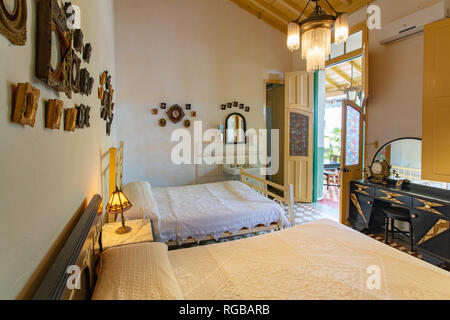 Camera da letto in stile coloniale con due letti antichi e pareti decorate con numerosi dipinti Foto Stock