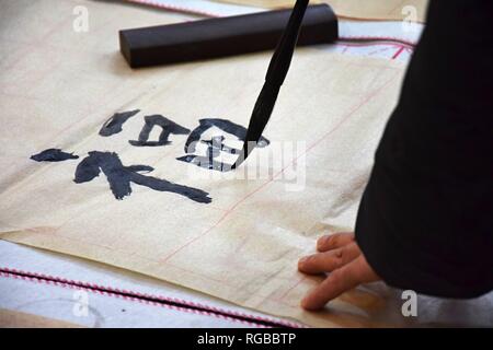 Una mano che tiene un pennello e la scrittura di un carattere cinese fu, la felicità. La pratica di calligrafia su un foglio di formazione di carta fragile. Foto Stock