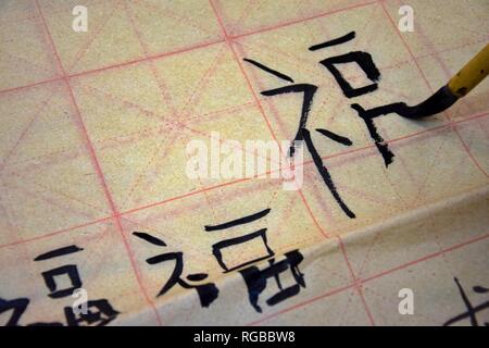 Una mano che tiene un pennello e la scrittura di un carattere cinese fu, la felicità. La pratica di calligrafia su un foglio di formazione di carta fragile. Foto Stock