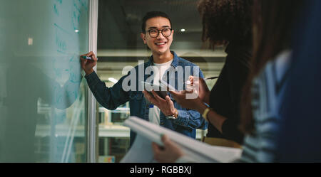 Studente iscritto sulla scheda di vetro in aula. Maschio di studente iscritto a bordo durante lo studio di gruppo in classe. Foto Stock