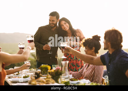 Bella coppia Giovane essendo saluto da parte di amici sulla loro gravidanza durante una festa. Gruppo di amici sollevando un brindisi per la gravidanza giovane a cena par Foto Stock