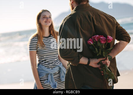 Coppia giovane in amore romantico data. Uomo con sorpresa mazzo di rose per la bella giovane donna sulla spiaggia. Foto Stock