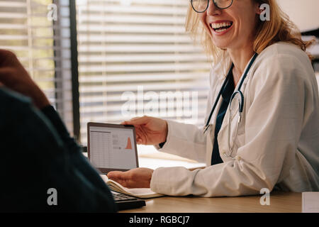 Medico donna che mostra i risultati del test per paziente e sorridente. Medico femmina felice con il recupero del suo paziente. Foto Stock