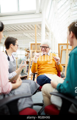 Ritratto di gioiosa arte maturo maestro parlando al gruppo di studenti seduti in cerchio in art studio Foto Stock