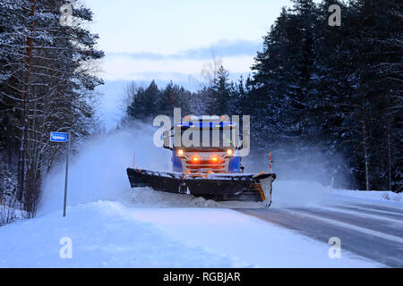 Salo, Finlandia - 18 Gennaio 2019: Blu Scania carrello equipaggiato con spartineve cancella un snowy fermata bus dall'autostrada nel sud della Finlandia in inverno al tramonto. Foto Stock