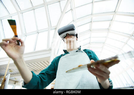 Angolo basso Ritratto di giovane uomo che indossa le cuffie VR pittura immagine sotto avveniristico tetto di vetro, spazio di copia Foto Stock