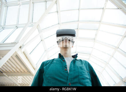 Angolo basso Ritratto di giovane uomo che indossa le cuffie VR in piedi sotto avveniristico tetto di vetro, spazio di copia Foto Stock