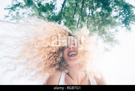 Ritratto di felice giovane donna con i riccioli biondi a retroilluminazione Foto Stock