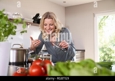 Donna sorridente cottura in odore di cucina al recipiente di cottura Foto Stock