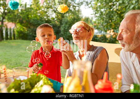 Nonna e nipote di soffiaggio bolle di sapone su un party in giardino Foto Stock