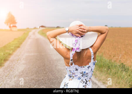 Vista posteriore della donna matura indossando hat su remoto paese lane in estate Foto Stock