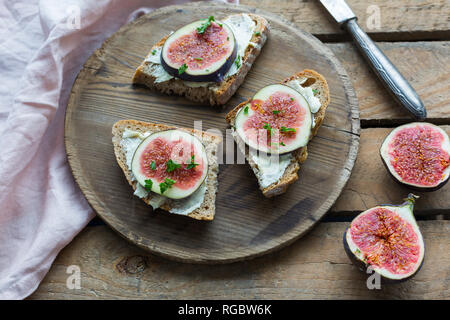 Fette di pane imburrate con spicchi di fichi sul piatto di legno Foto Stock