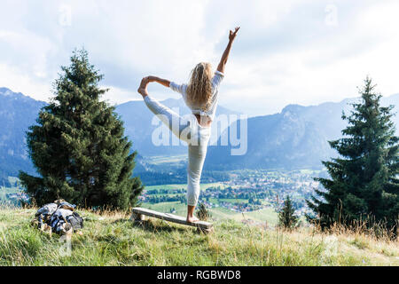 In Germania, in Baviera, Oberammergau, giovane donna fare yoga su banco sul prato di montagna Foto Stock